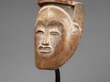 a wooden mask on a stand with a gray background