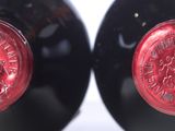 two bottles of red wine are sitting side by side on a white surface