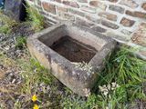 un abreuvoir en pierre posé dans l'herbe, près d'un mur de briques