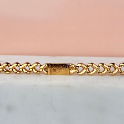 un bracelet en or muni d'un fermoir en forme de cœur, posé sur une surface en marbre
