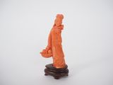 une figurine orange représentant un homme tenant un poisson, posée sur un socle en bois