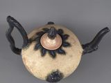 a teapot with a flower on it on a gray surface
