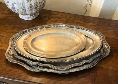 trois assiettes en argent posées sur une table en bois, avec un vase en arrière-plan