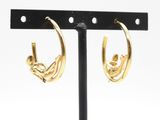 une paire de boucles d'oreilles créoles dorées posées sur un support en métal noir