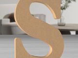 a wooden letter s on a table with a vase in the background