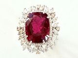 une photo d'une bague sertie d'un rubis et de diamants posée sur une surface blanche
