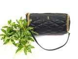black quilted purse with gold chain strap next to a green plant