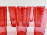 six red drinking glasses are lined up on a white surface