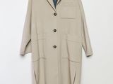 un manteau beige suspendu à un cintre devant un mur blanc