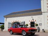 an old red car parked in front of a building with a blue sky in the background