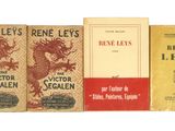 Trois livres sont alignés sur une surface blanche, dont l'un a une couverture rouge.