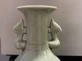 a green vase sitting on a table next to a white wall