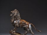 une statue en bronze représentant un lion, posée sur un socle en bois