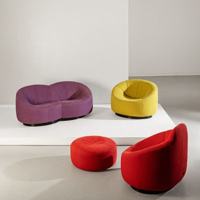 Plusieurs chaises de différentes couleurs sont disposées sur une estrade blanche dans une pièce