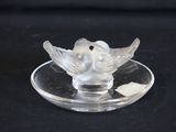 un oiseau en verre posé sur une assiette en verre, sur fond noir