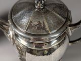 a silver tea pot with a lid and a spoon