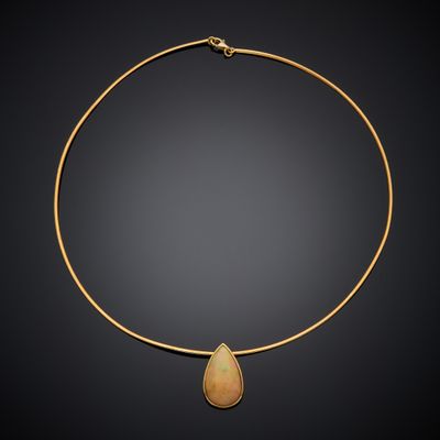 a gold necklace with a tear shaped stone on a black background