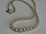 un collier de perles blanches muni d'un fermoir en or, posé sur un fond blanc