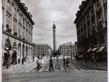 photographie en noir et blanc montrant des personnes traversant la rue devant une tour horloge