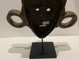 a wooden mask on a black stand on a white surface