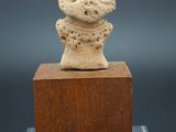 une petite statue en pierre représentant un homme coiffé d'un chapeau, posée sur un bloc de bois