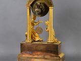 a gold clock with a woman holding a pendulum