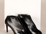 une paire de bottines en cuir noir posées devant une boîte blanche