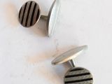 une paire de boutons de manchette rayés argent et noir sur un fond blanc
