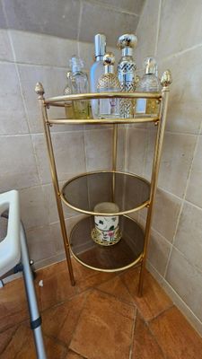une étagère dorée dans un coin de la salle de bains, sur laquelle sont posés des flacons