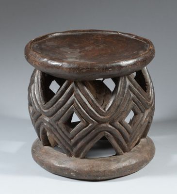 un vieux tabouret en bois dont l'assise est ornée d'un motif sculpté