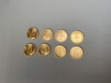 six pièces d'or sont disposées en ligne sur une surface grise