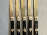 four knives with black handles and gold accents on a white surface