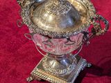 an antique silver plate with a lid on a stand on a red carpet
