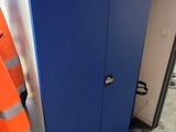 a man in an orange safety vest standing next to a blue cabinet