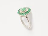 a close up of a ring with green stones on a white surface