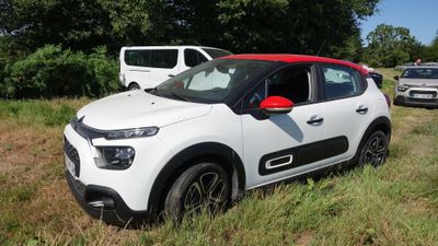 une petite voiture blanche garée dans un champ, à côté d'une camionnette