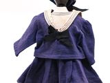 poupée vêtue d'une robe violette et d'un chapeau, posée sur un socle noir