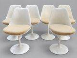four white tulip chairs with beige cushions on a grey surface