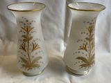 deux vases blancs ornés de motifs dorés, posés sur un tissu blanc