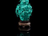 un vase en jade vert sculpté, posé sur un socle, sur fond noir