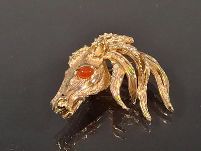 a gold horse head brooch on a black surface
