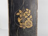 an old book with gold flowers on it sitting on a white surface
