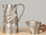 a silver pitcher next to a silver cup on a wooden table