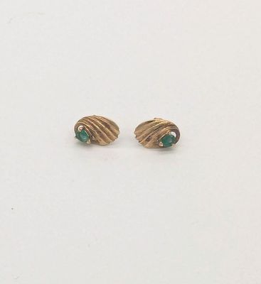 une paire de boucles d'oreilles en or et émeraude posées sur un fond blanc