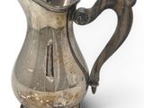 an old silver pitcher with a handle on a white surface