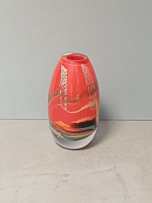 un vase rouge posé sur une table, avec un mur gris en arrière-plan