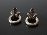 two silver earrings with black stones on them sitting on a black surface