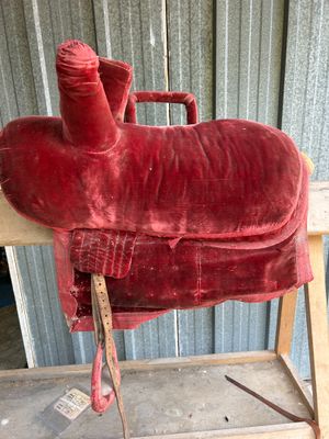 a red horse saddle sitting on top of a wooden bench
