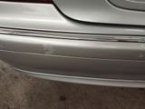 the rear end of a silver car with scratches on it ' s bumper