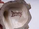 a hand holding a small porcelain object with writing on it